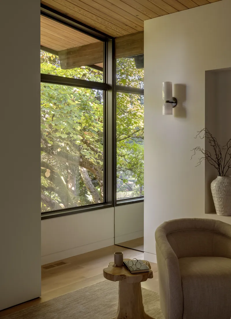 Corner seating area with timber ceiling and black-framed windows overlooking green summer foliage