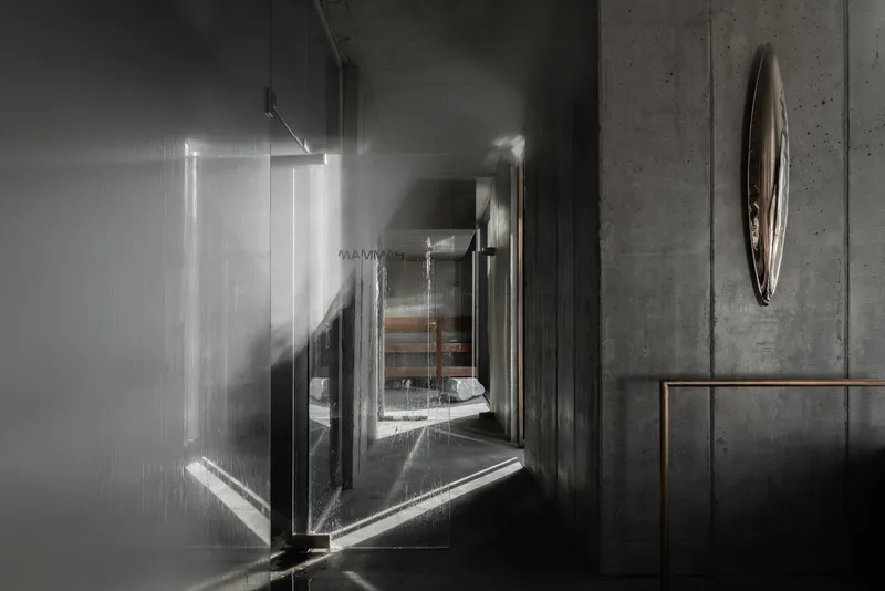 Corridor with glass panels and concrete walls casting angular shadows from overhead track lighting