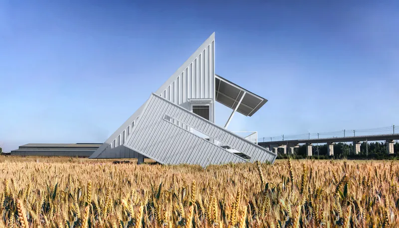 White corrugated metal pavilion with angled roof planes rising above a golden wheat field