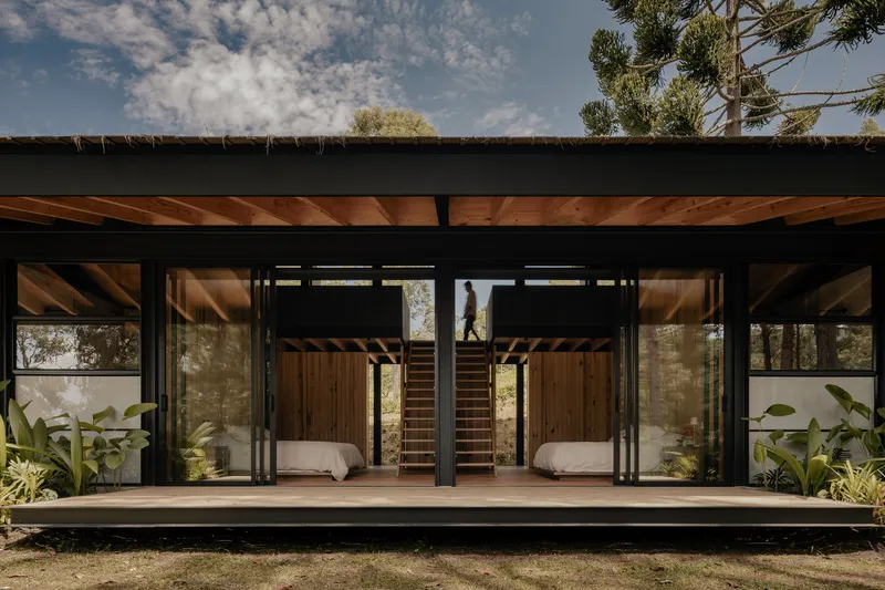 Front elevation showing sliding glass doors and central staircase beneath exposed timber ceiling beams and black steel frame