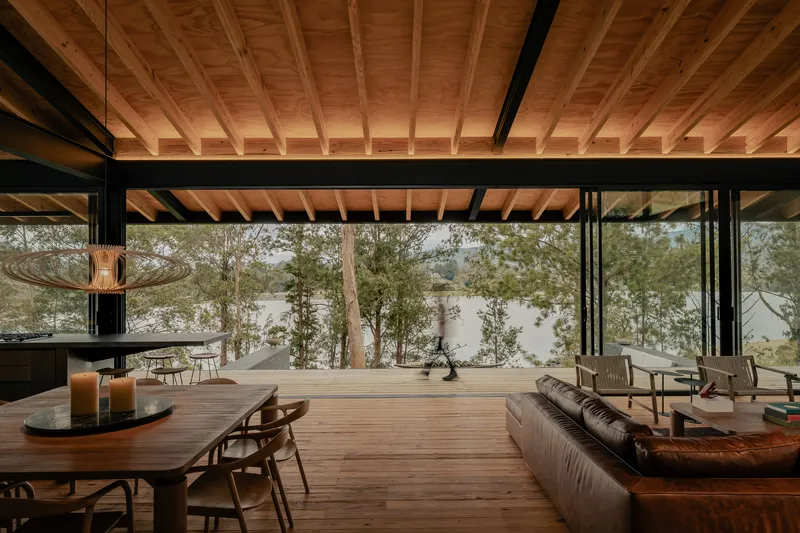 Open living space with exposed timber ceiling joists and full-height glazing framing lakeside trees