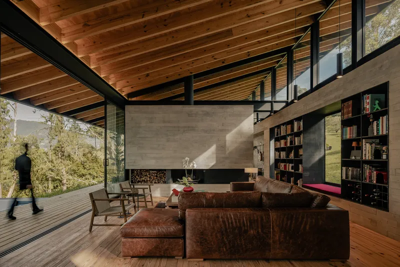 Living room with board-formed concrete fireplace wall and figure walking onto the timber deck
