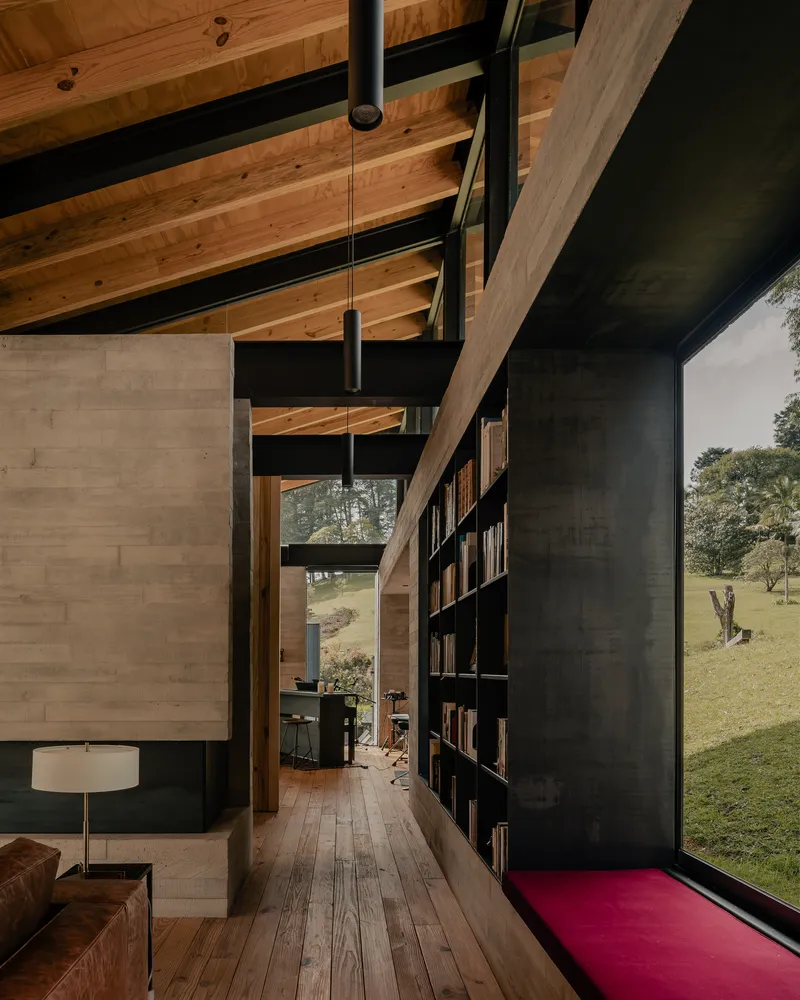 Hallway passage with black steel bookshelf wall and glimpse of the grassy clearing beyond