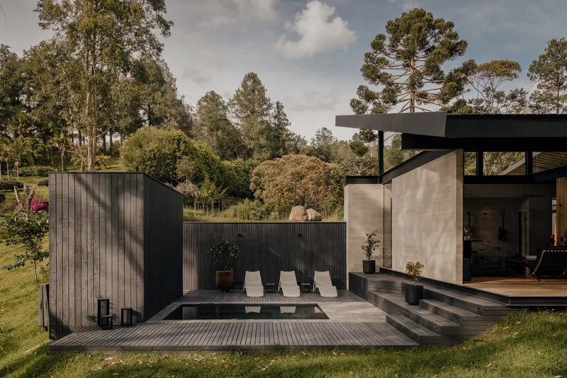 Timber deck with sunken pool flanked by blackened wood walls and concrete volumes under afternoon light