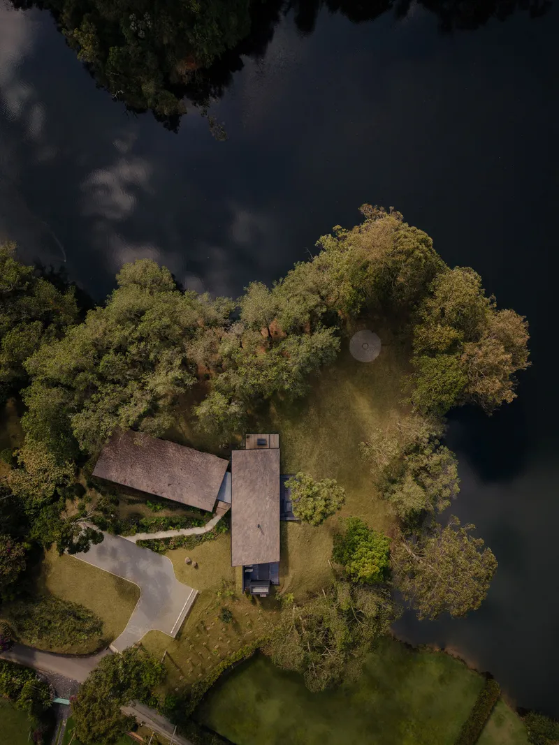 Aerial view of three linear volumes on a forested peninsula extending into dark water