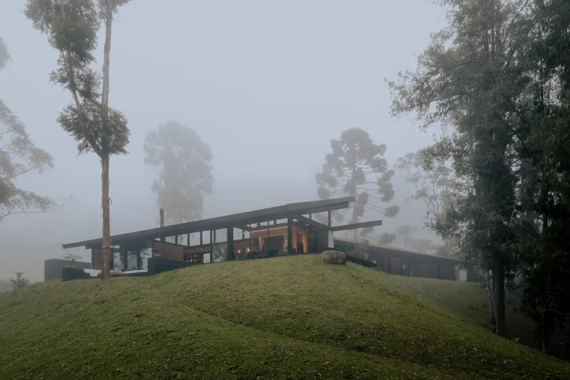 Hillside pavilion with extended flat roof and glazed walls emerging from dense fog