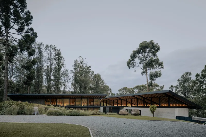 Entry approach showing the sloped roof canopy over timber-clad and glazed facades at dusk