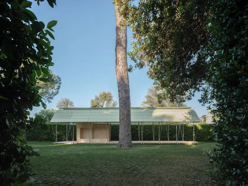 Long view of the translucent curved pavilion roof sheltering a glass enclosure on a lawn between tall trees