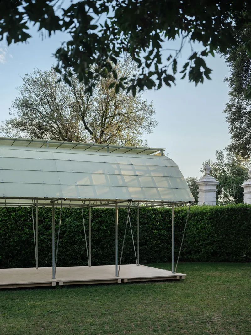 Translucent pavilion roof on slender steel columns set in a garden framed by overhanging tree branches