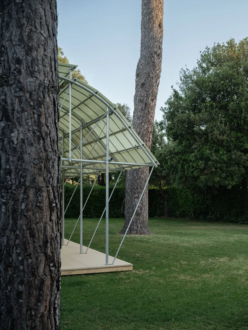 Garden pavilion with folded canopy threading between pine trees at dusk with trimmed hedges beyond