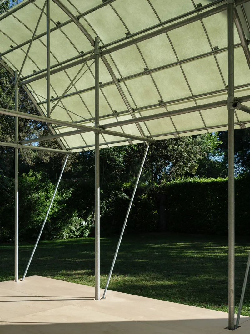 View beneath the tensile canopy showing slender angled steel supports and gridded fabric panels filtering daylight