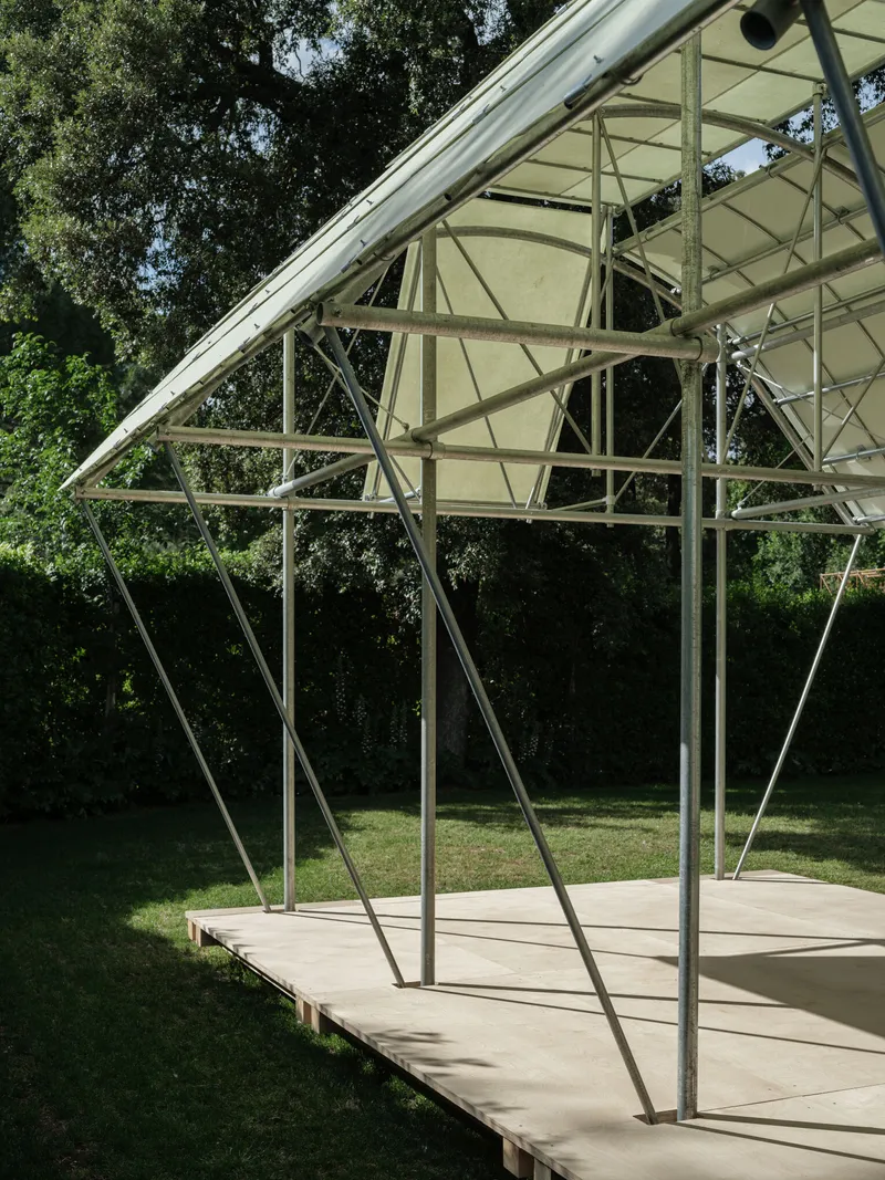 End elevation of the pavilion revealing the curved steel trusses and diagonal bracing against dense foliage