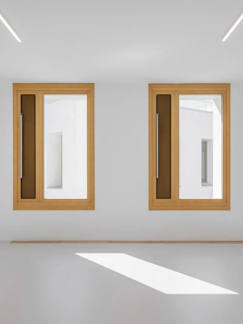 Two timber-framed windows with narrow sidelights and a sharp trapezoid of sunlight on the floor