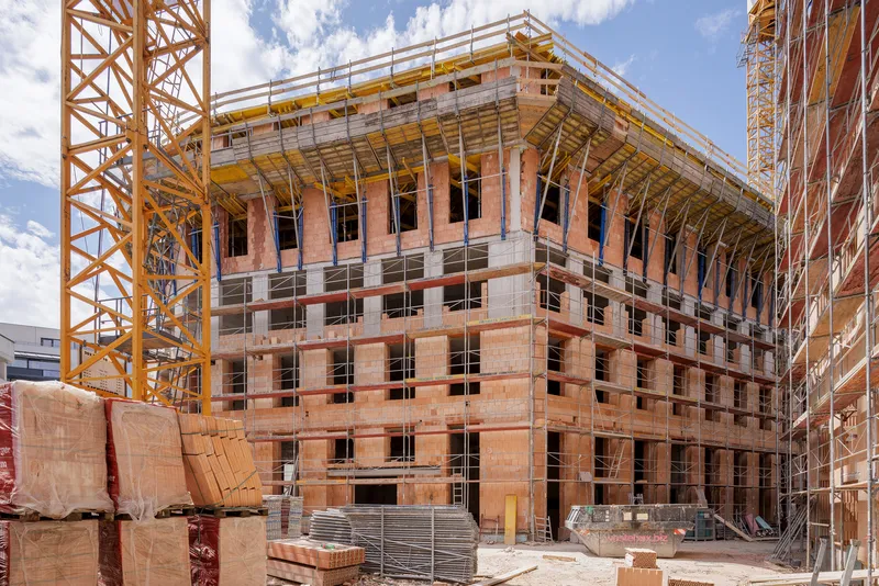 Construction site view of the terracotta block structure with timber framing under yellow tower cranes