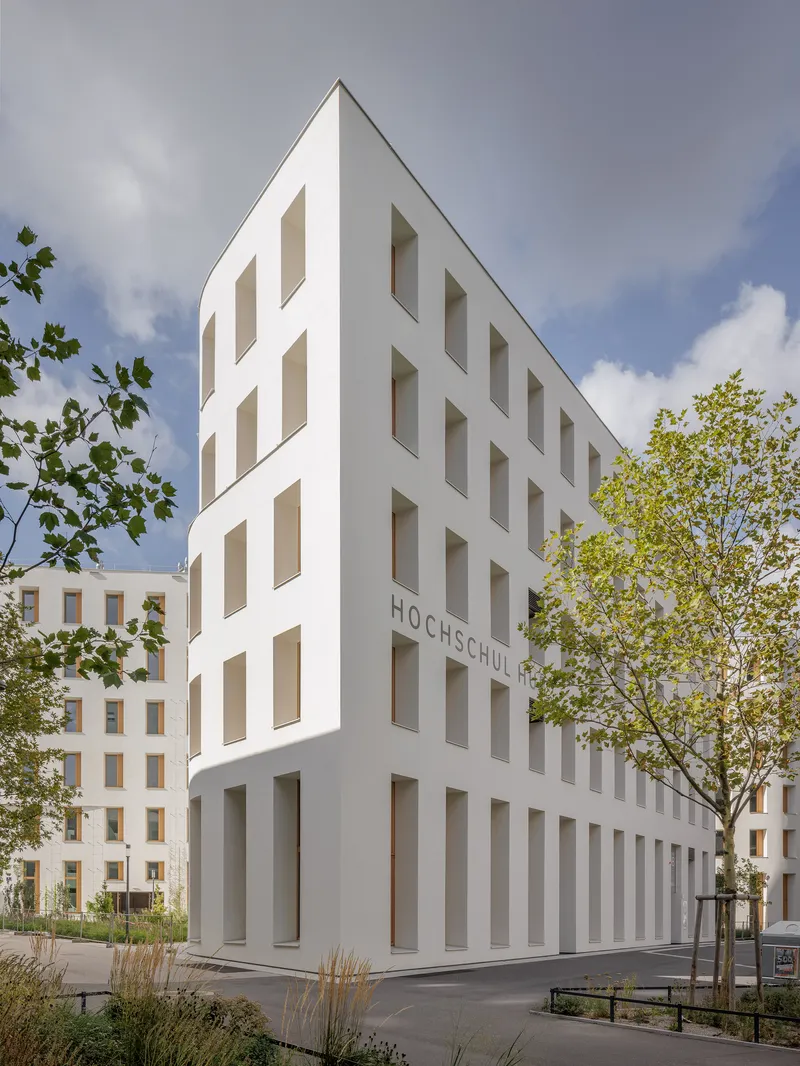 Sharp corner facade rising five stories with recessed windows under a partly cloudy sky