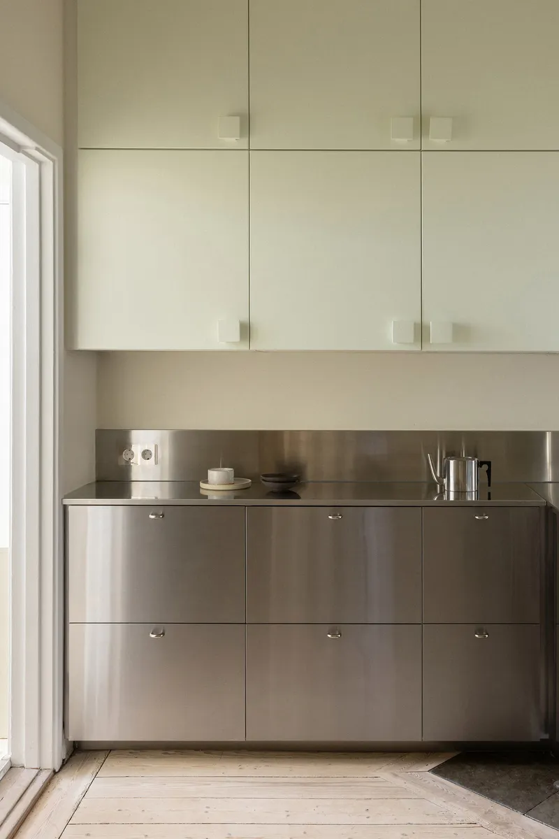 Kitchen counter with brushed stainless steel base cabinets below pale upper cabinetry and a window