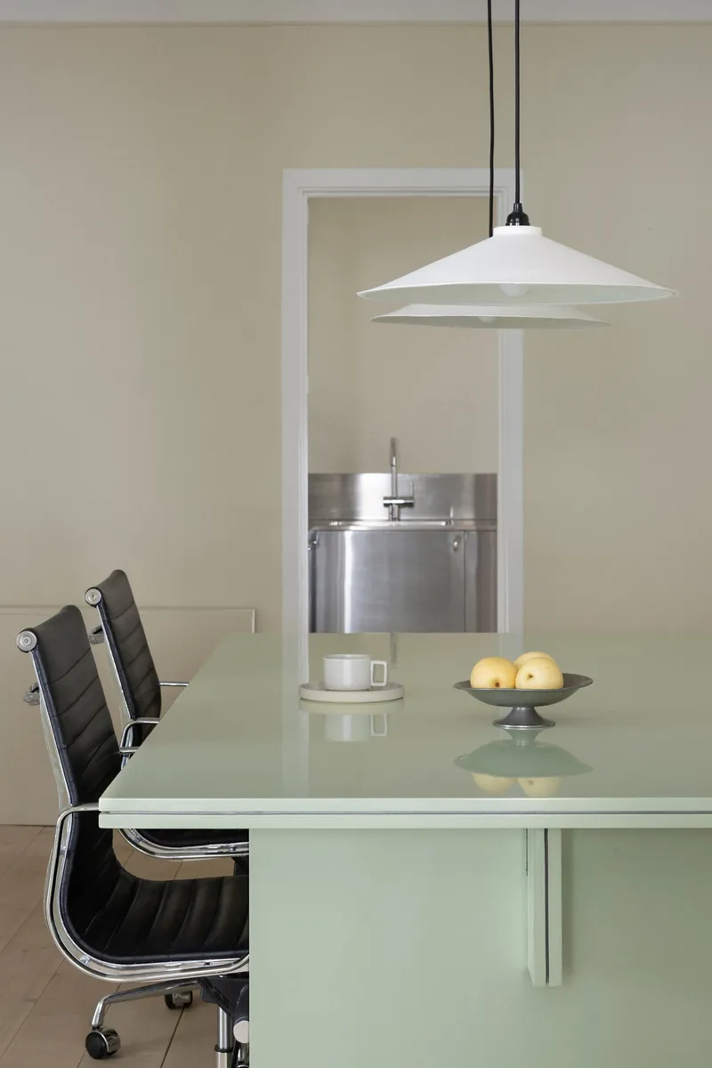 Glass dining table with white pendant lamp and a view through to the stainless kitchen