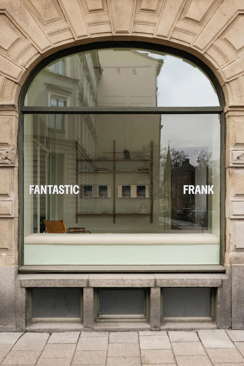 Arched storefront window with black steel frame set within rusticated stone facade under overcast sky