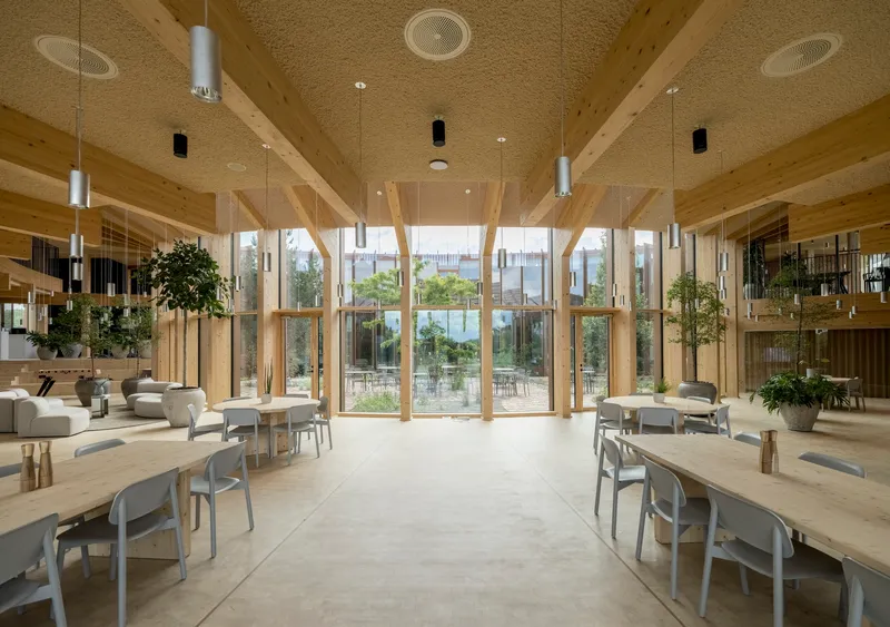 Double-height dining hall with exposed timber framing and pendant lights overlooking a planted courtyard