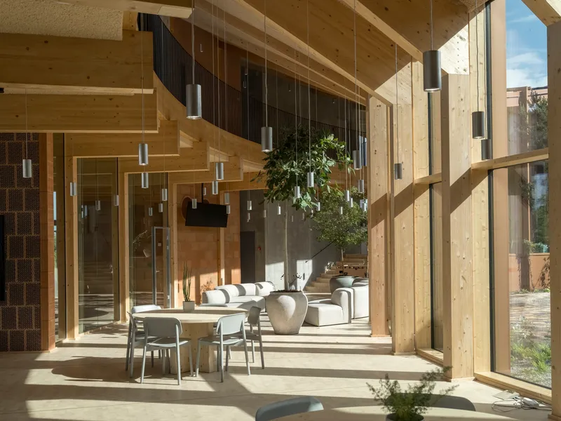 Corner seating area with sunlight casting shadows through the timber structural frame and glazed walls