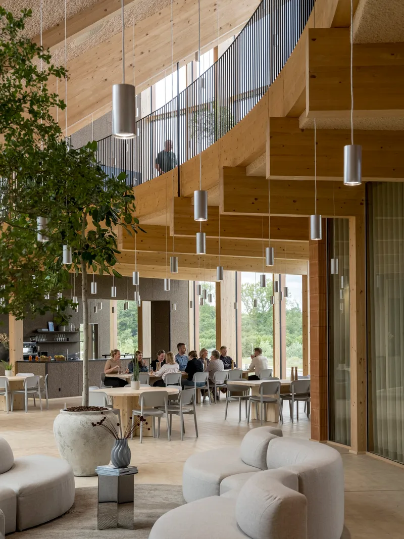 Double-height interior showing vertical metal slat balustrade and potted trees beneath suspended cylindrical pendants