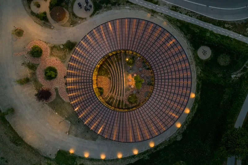 Aerial view of circular brick amphitheater with concentric rings of paving illuminated at twilight