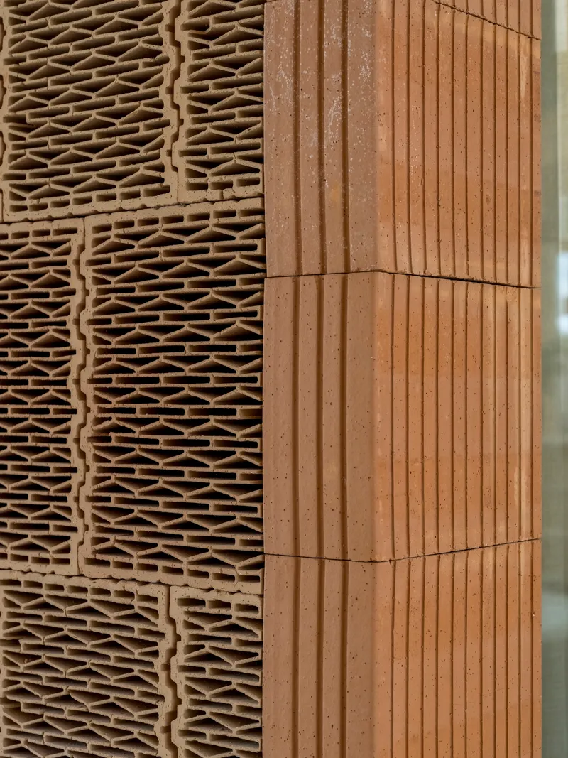 Detail junction of ridged terracotta panel meeting corrugated timber cladding at an angle
