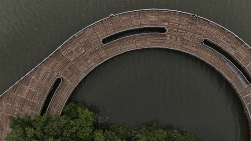Curved timber boardwalk with elongated openings arcing over still water near vegetation