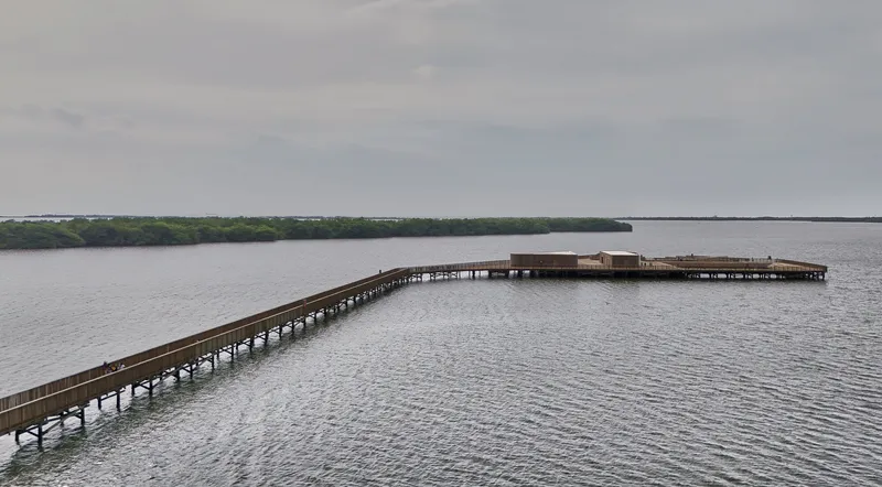 Elevated timber boardwalk extending across open water toward distant viewing pavilion under overcast sky