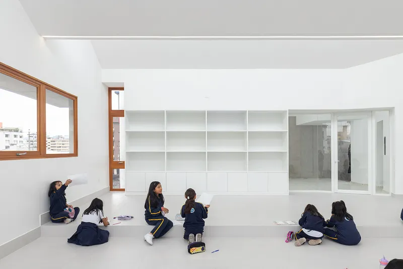 Classroom with built-in white shelving and timber-framed windows as students gather on the floor