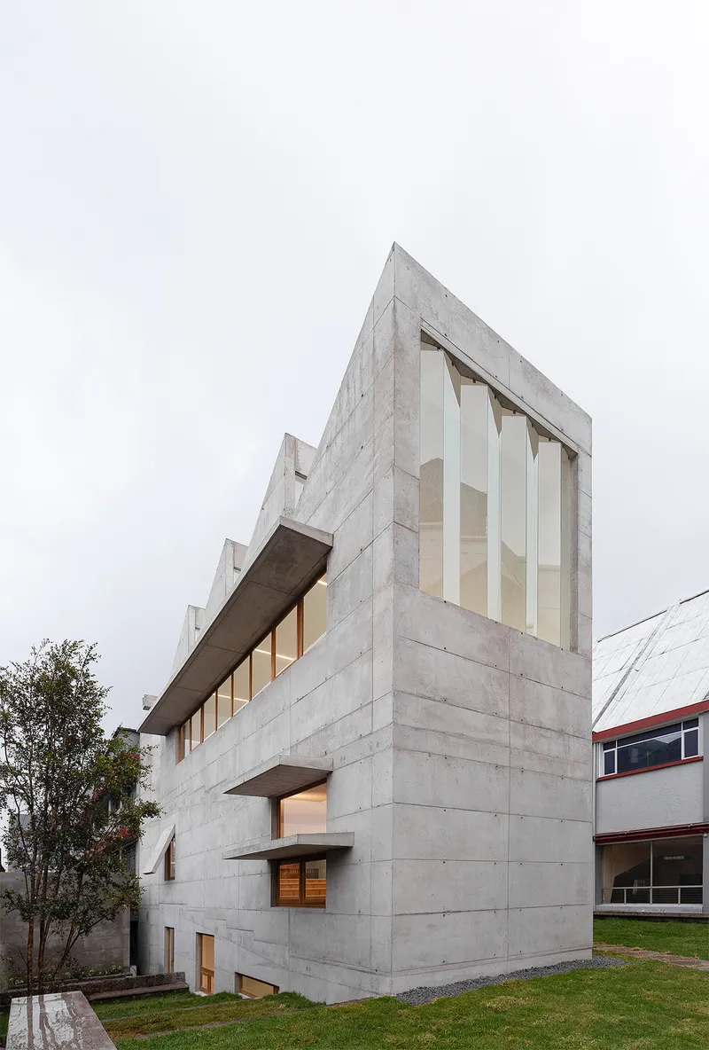 Corner view of the board-formed concrete volume with vertical window openings under overcast sky