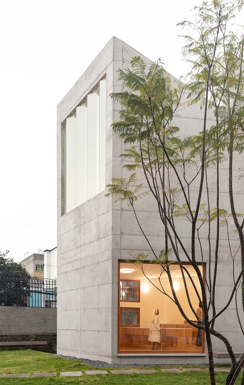 Tall concrete volume with floor-to-ceiling glass and slender trees framed against the facade at dusk
