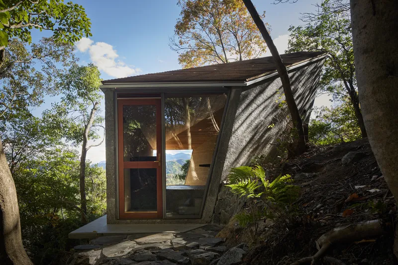 Entrance facade with angled glass doors and board-formed concrete walls on a hillside slope