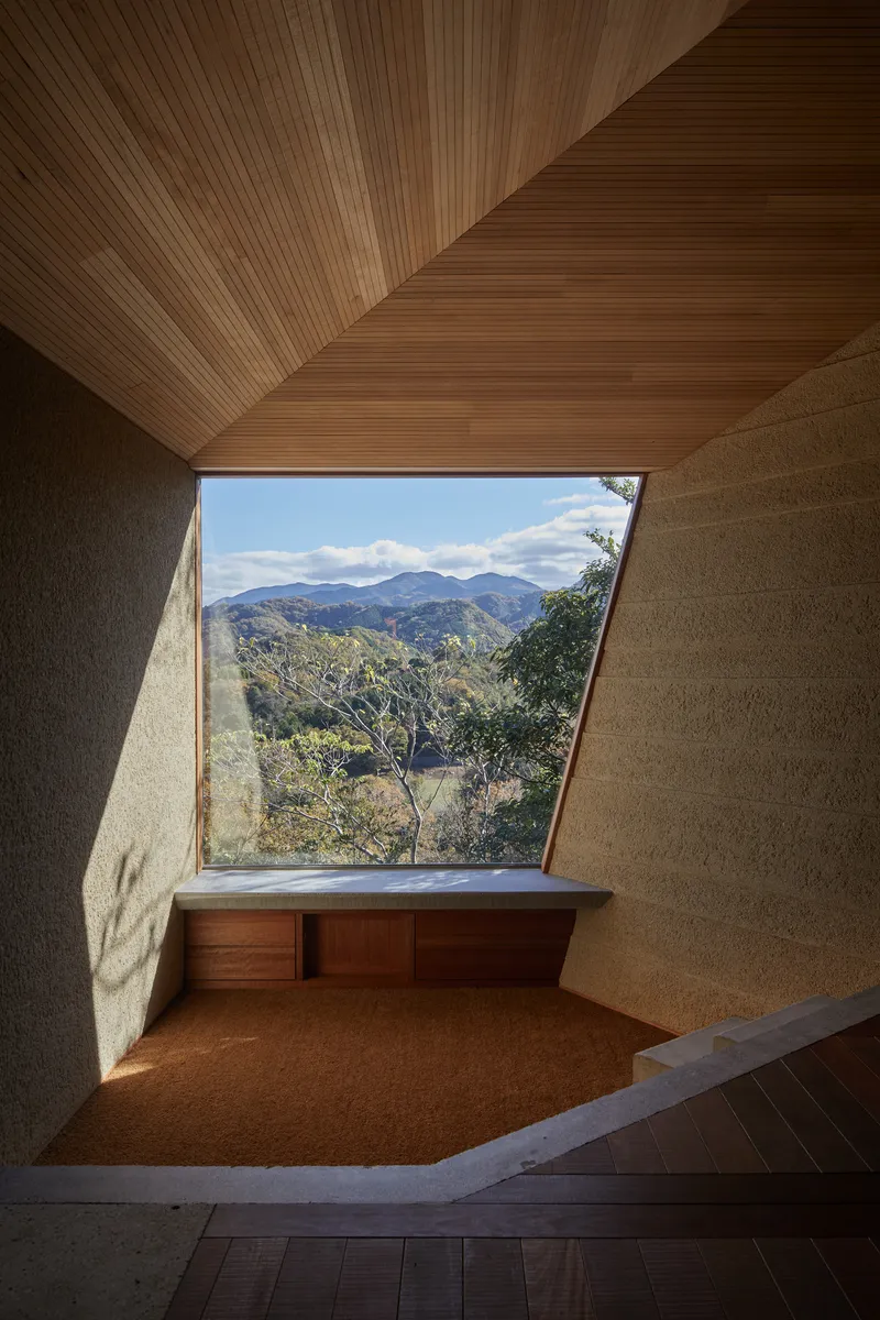 Built-in timber bench beneath an angled window framing distant mountains under blue sky