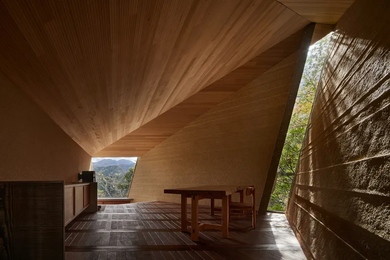 Interior showing ribbed timber ceiling planes converging above stone walls and a framed mountain view