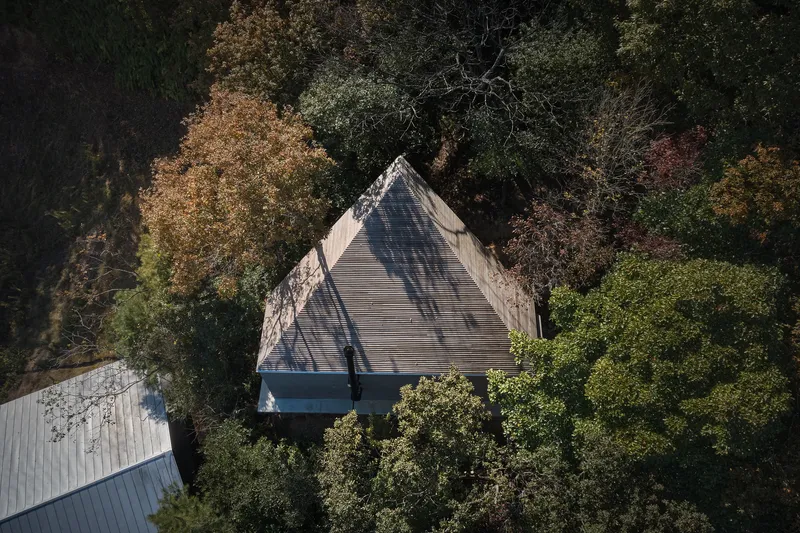 Aerial view of the peaked metal roof nestled among deciduous trees in autumn foliage