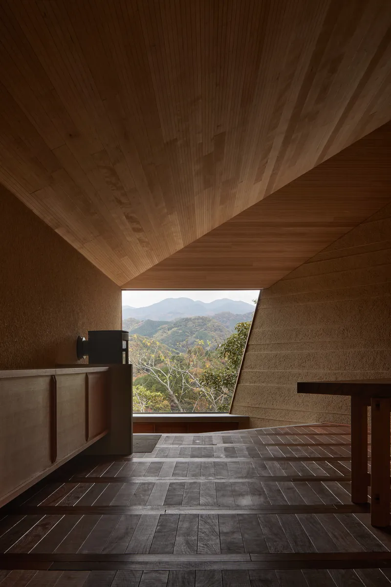 Interior with timber-lined ceiling and angled window framing distant mountains and forest canopy
