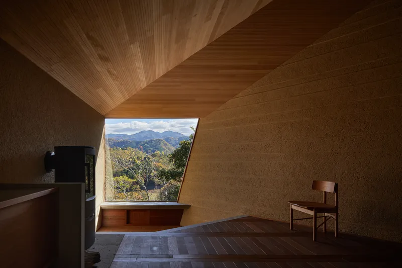 Angled window seat beneath timber ceiling with view to forested hillside and distant peaks