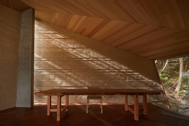 Timber bench against textured stone wall beneath angled ceiling with filtered sunlight