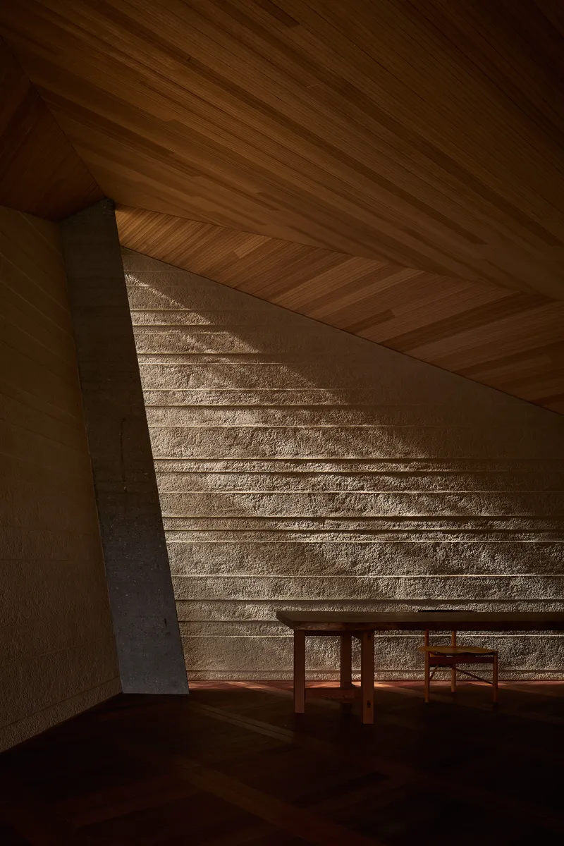 Corner detail showing timber ceiling meeting textured stone wall with diagonal afternoon light