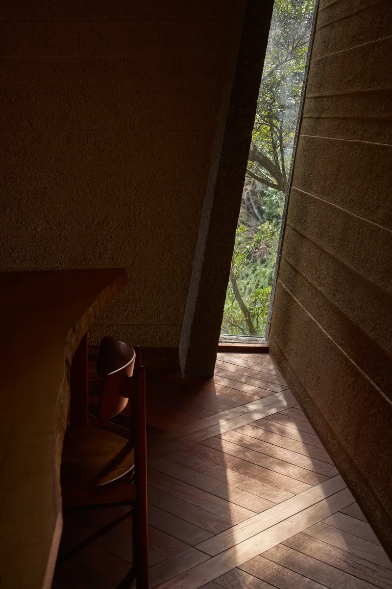 Narrow vertical window slot framing trees between textured stone walls and timber flooring