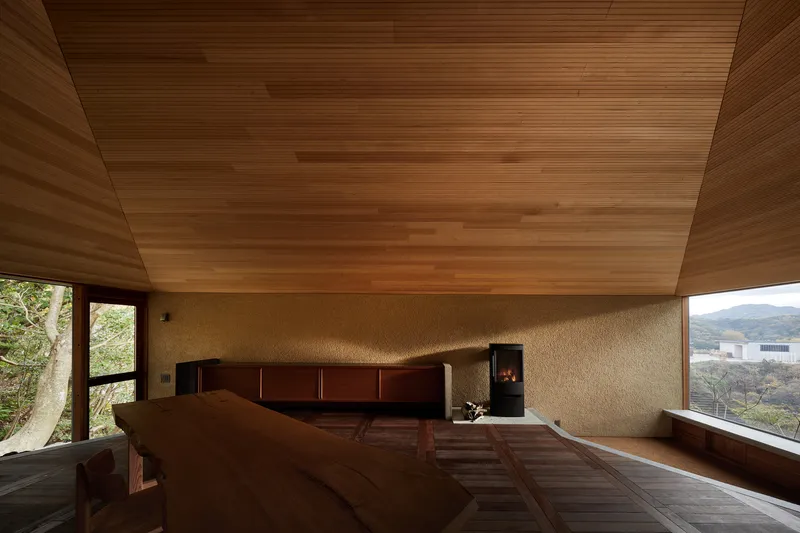 Bedroom interior with timber plank ceiling and stone walls overlooking forested hillside through corner windows
