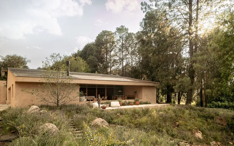 Single-story rammed earth structure with pitched roof set among native grasses and tall trees