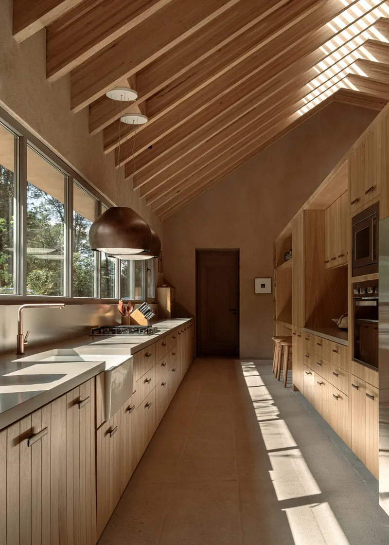 Galley kitchen with timber cabinetry and vaulted ceiling illuminated by slanting afternoon light