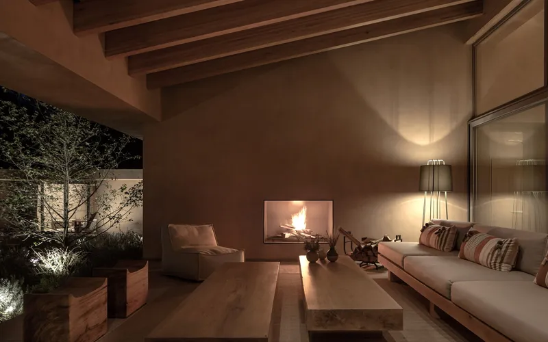Living room at night with fireplace glowing and uplighting on illuminated courtyard trees