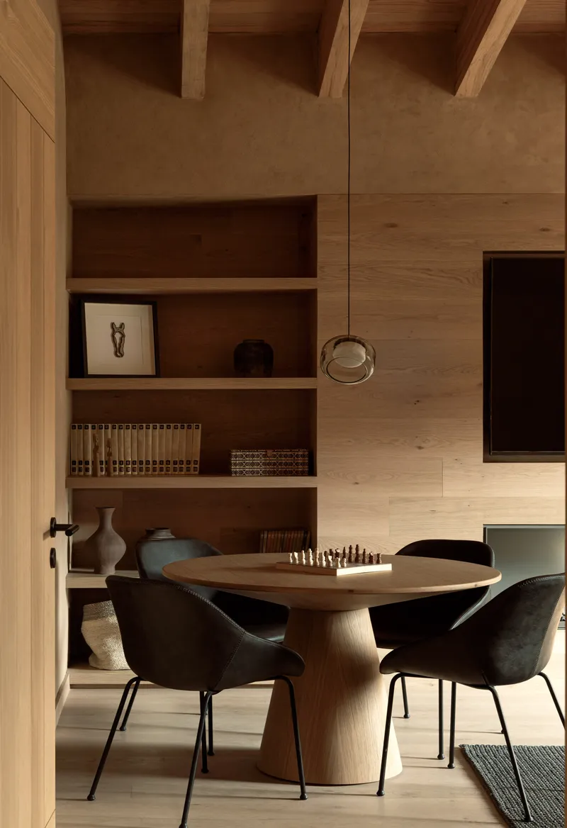 Dining area with curved timber pedestal table and built-in shelving beneath exposed timber beams and ceiling