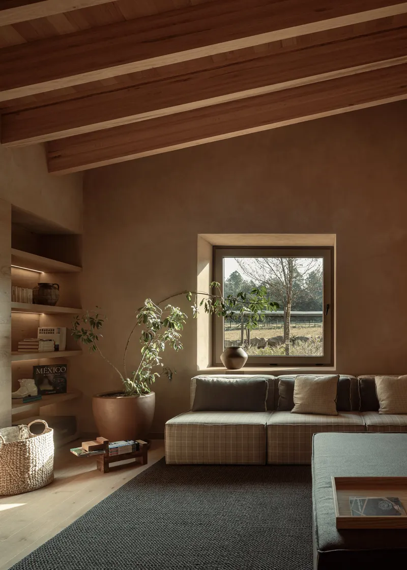 Living room with deep window seat overlooking bare winter trees and timber ceiling beams with plaster walls