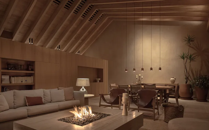 Open-plan living and dining space with exposed timber rafters and a central fire pit at dusk