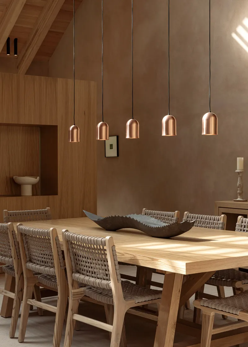 Dining table with woven chairs under a row of copper pendant lights in warm afternoon sun