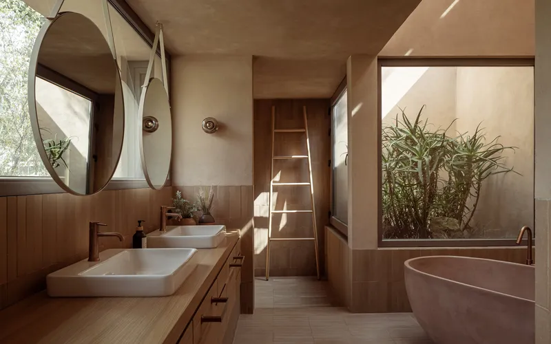 Bathroom with double vessel sinks, round mirrors, and indoor planted courtyard in morning light